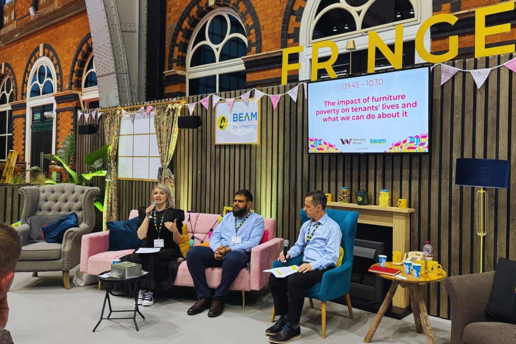 Aileen and fellow seated panellist at the fringe stage at the housing 2024 event. Aileen is holding a mic as she speaks at the event as she discussed finding solutions through flooring provision at the point of let