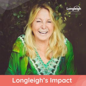 A cheerful woman depicting grantee Lyndsay, with long blonde hair wearing a green embellished top smiles brightly against a leafy background. The Longleigh Foundation logo is in the top right corner, and the text "Longleigh's Impact" is displayed in bold white font on a red banner at the bottom.